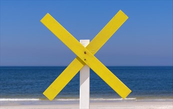 A yellow wooden cross marks a shoal near the shore at the beach