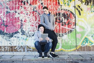 Casual and relaxed young man and woman reading on a notepad in front of grafitti wall in urban area