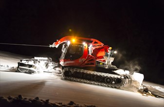 Snowcat planing ski slope with rope at night