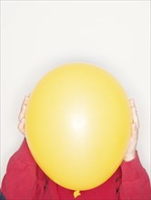 Child holding a yellow balloon in front of face
