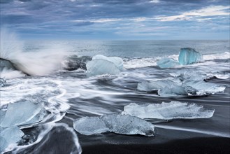 Pieces of ice on the black beach lapped by the sea