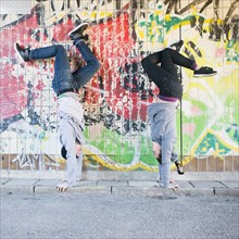 Young man and woman doing handstand in front of grafitti wall in urban area
