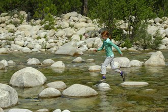Girl jumping over rocks in the river Solenzara