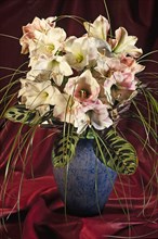 Bouquet of lilies in a vase in front of red fabric