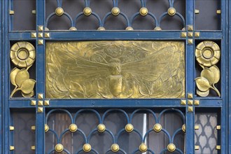 Gold-coloured relief of a bee at a wrought-iron gate around 1900