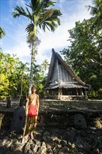 Traditionally dressed boy standing in front of a traditional hut