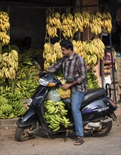 Man on scooter by a banana stand