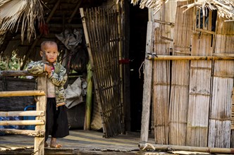 Child from the Lahu people standing outside a bamboo hut