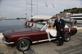 Bride and groom posing with an open Ford Mustang convertible car at a harbour