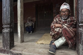 Nepalese man wrapped in a blanket sitting at an entrance