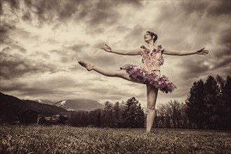 Ballerina wearing a tutu dances in front of a cloudy