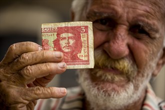 Elderly Cuban man holding a 3-peso bill with the portrait of Ernesto Che Guevara in his hand