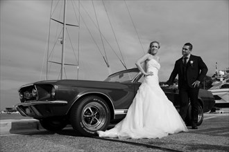 Bride and groom posing in front of a Ford Mustang at a harbour