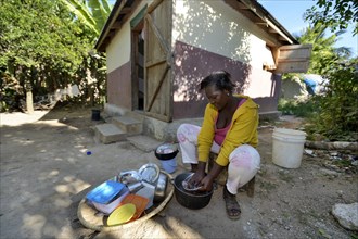 Young woman washing the laundry in front of the house which was given to the family by a relief organisation