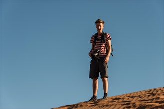 Teenager with photo camera standing on a dune