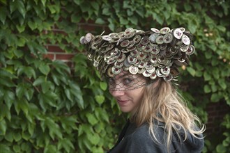 Young woman wearing a hat made of crown corks in front of a wall of leaves