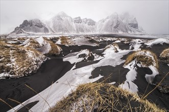Snow on black sand dunes in front of Vestrahorn mountain in winter