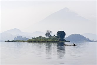 Canoe glides in the morning mist on Mutanda Lake in front of Muhavura volcano at the border with Rwanda