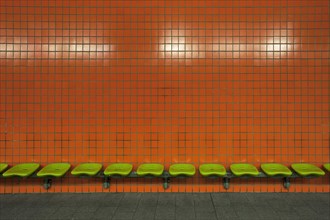 Green seats in front of an orange tiled wall in an underdground station