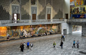 Visitors looking at the murals in the main hall of Oslo City Hall