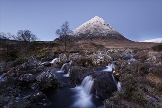 View of moorland with small waterfalls in rocky stream and snow capped mountain in background at dawn