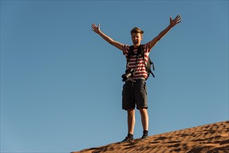 Teenager with photo camera standing on a dune and spreading his arms