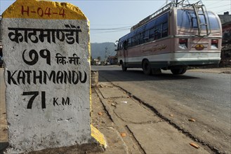 Milestone at the roadside with a Nepalese bus passing