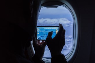 Silhouette of a man taking photos of the mountains using a smartphone from an airplane window