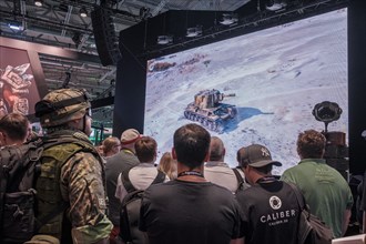 Visitors in military clothing watching a war game on a video wall at Gamescom