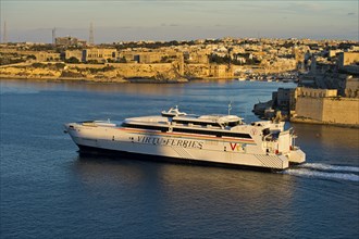 Jean de la Valette ferry of the Virtu Ferries shipping company passing the fortress Fort St. Angelo in the Grand Harbour