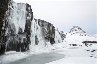 Mountain Kirkjufell behind frozen waterfall Kirkjufellsfoss in the snow