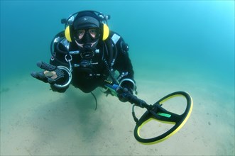 Diver with metal detector displays the ancient coins he found