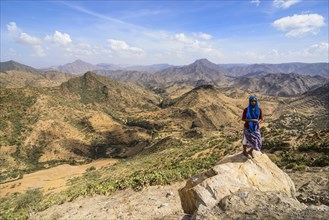 Local woman standing on a rock in front of the mountain scenery along the road from Massawa to Asmarra