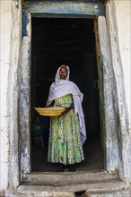 Friendly old woman standing with a basket of corn in a door frame