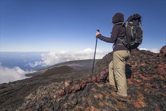 Hiker on the summit of the Piton de la Fournaise volcano with views of clouds and the sea