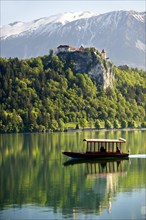 A flat bottomed boat called Pletna on Lake Bled with Bled Castle and the alps at the back