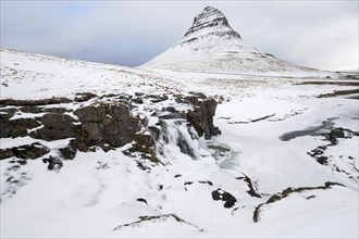 Mountain Kirkjufell behind frozen waterfall Kirkjufellsfoss in the snow