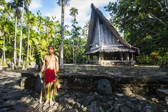 Traditionally dressed boy standing in front of a traditional hut