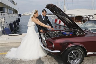 Bride and groom looking into the engine compartment of a Ford Mustang after a breakdown