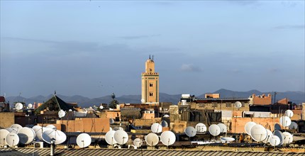 View across the roofs with satellite dishes to a minaret and the Atlas Mountains