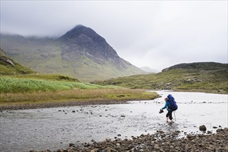 Woman with backpack crossing river Abhainn Camas Fhionnairigh