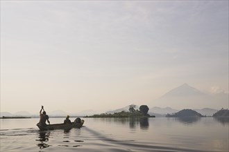Guide and woman in canoe in the morning mist by Mutanda Lake volcano in front of Muhavura