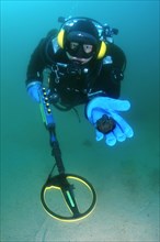 Diver with metal detector displaying found ancient coins