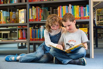 Two children reading reading a book in a public library