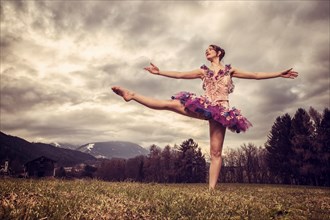 Ballerina wearing a tutu dances in front of a cloudy sky