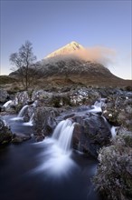 View of moorland with small waterfalls in rocky stream and snow capped mountain in background at dawn
