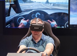 Visitor wears Virtual Reality glasses in a driving simulator for car racing at gamescom