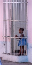 Girl behind window bars in a pink house