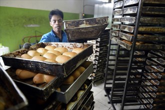 Young man in a bakery taking bread out of the oven