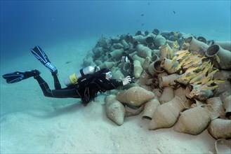 Underwater photographer photographing school of fish on amphora